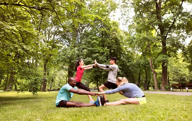 Group of friends exercising together outdoors, practicing partner stretches and balancing poses in a park